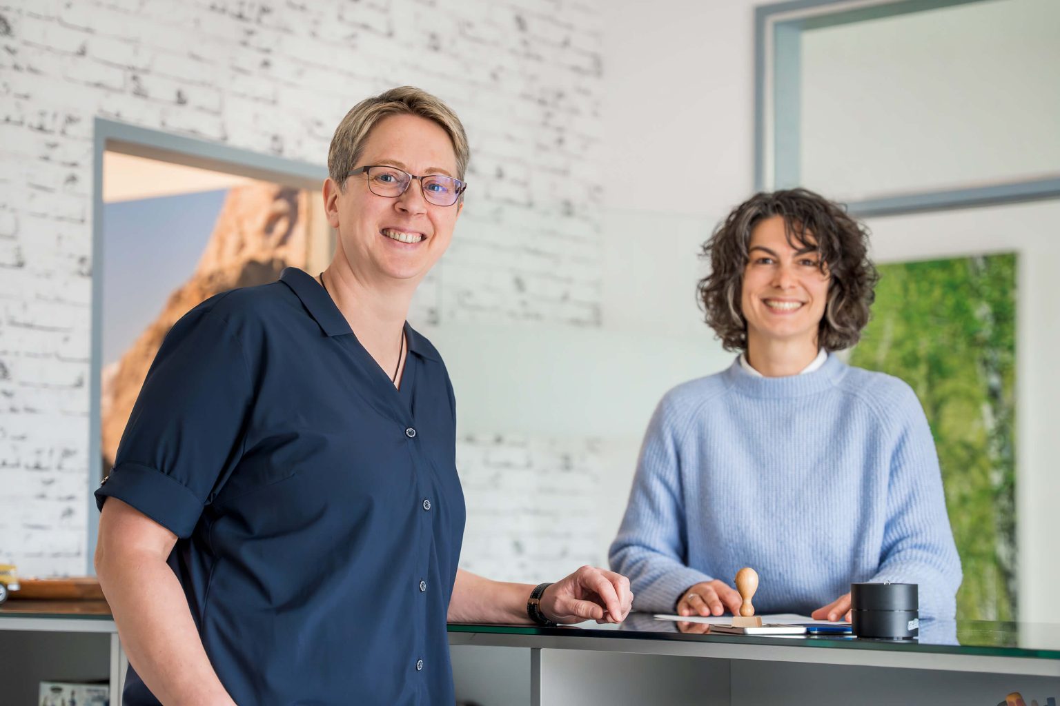 Zwei freundliche Empfangsmitarbeiterinnen stehen gemeinsam am Kundenservice-Tresen