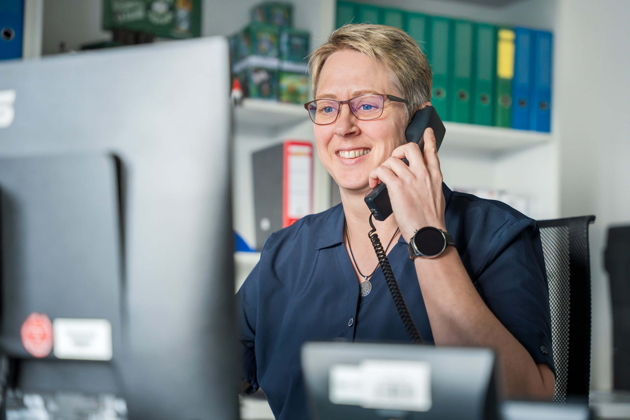 Lächelnde Rezeptionistin mit Brille führt freundliches Telefonat am Arbeitsplatz