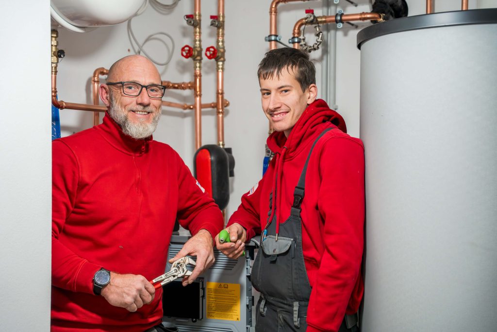 Zwei Heizungstechniker mit Werkzeug bei Installation eines Pufferspeichers