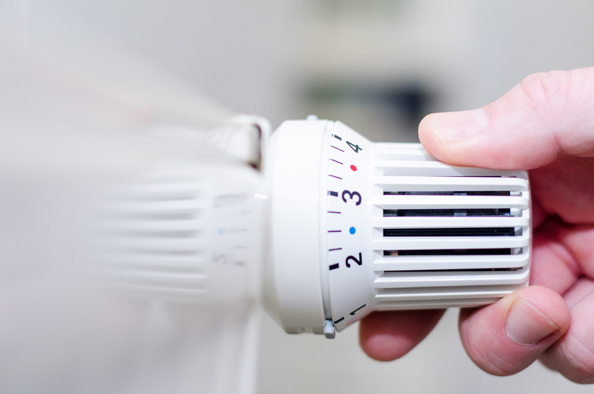 Nahaufnahme einer Hand, die an einem Heizkörper-Thermostat dreht